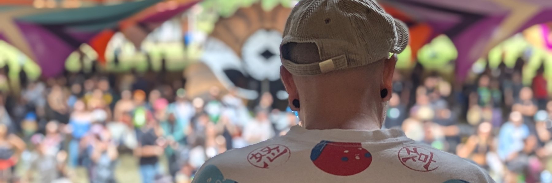 DylAlien facing a large daytime crowd beneath painted canopies.